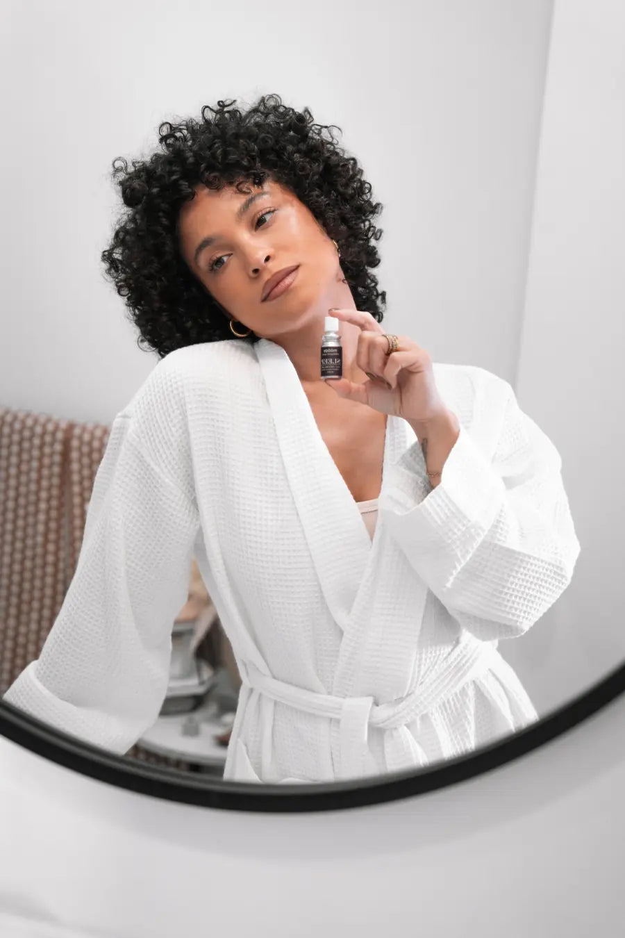 A woman in a white robe holding the SLEEP spray at the mirror